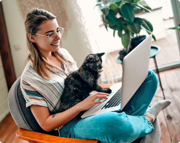 Woman wearing glasses using laptop with cat on her lap