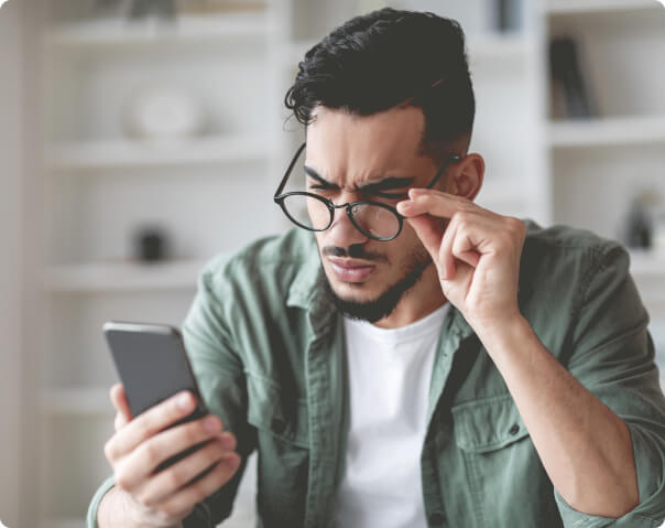 Man squinting holding glasses and using smartphone